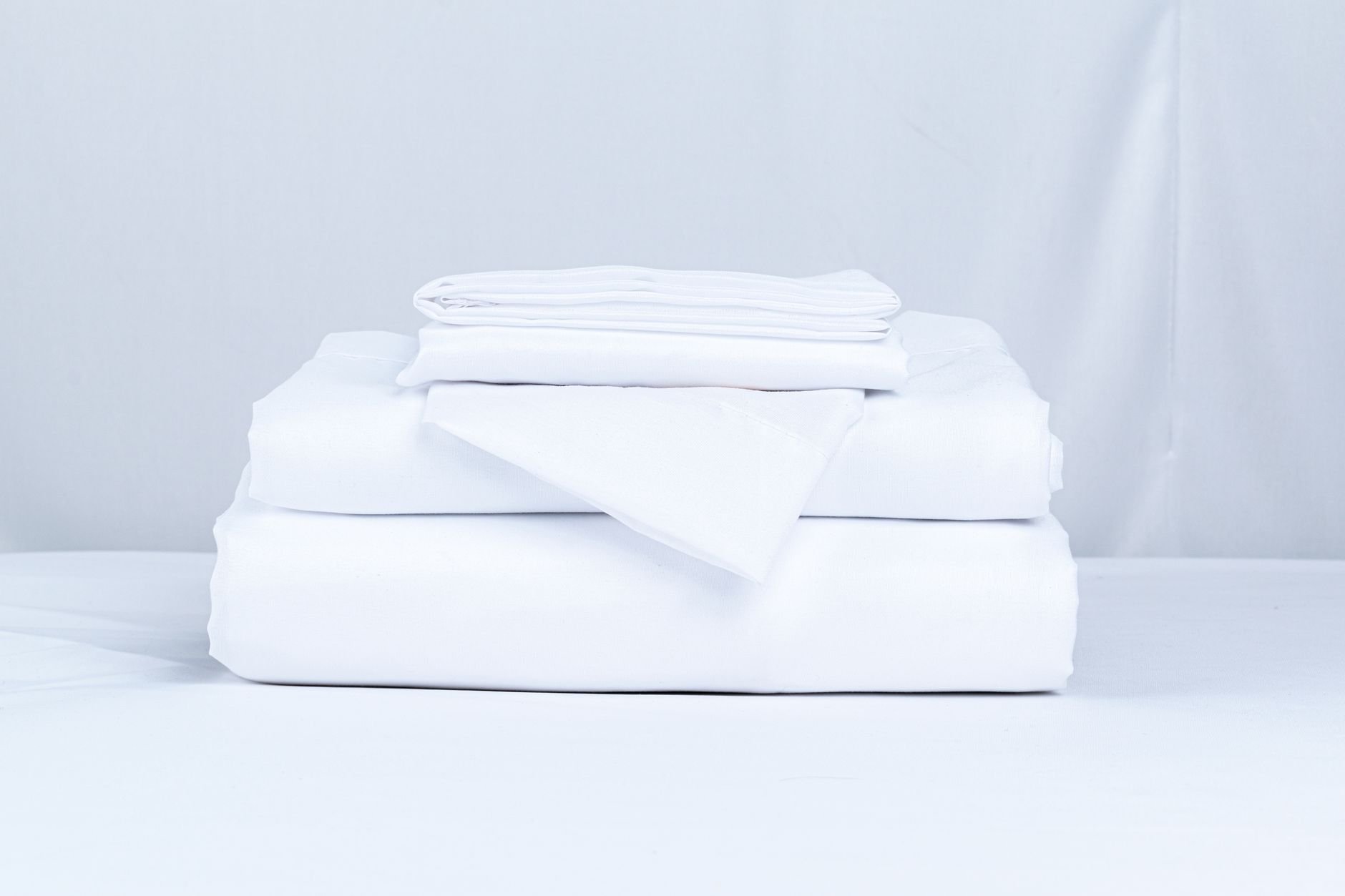 A neatly folded stack of crisp white bed linens on a clean surface.